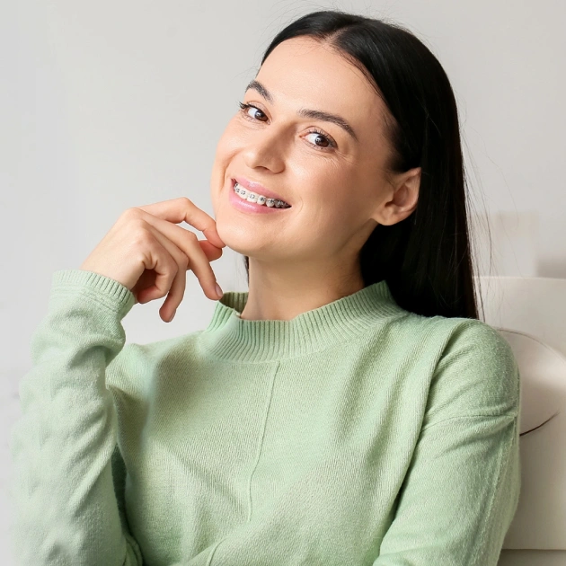 Woman in green sweater smiling, displaying healthy teeth in bright, welcoming orthodontic portrait.