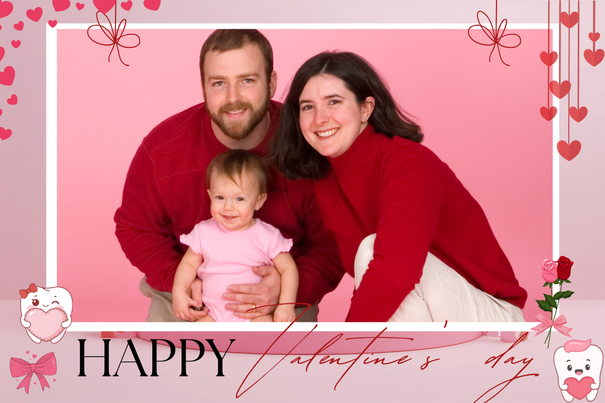 Family portrait with two adults and toddler in red clothing against pink Valentine's Day background.