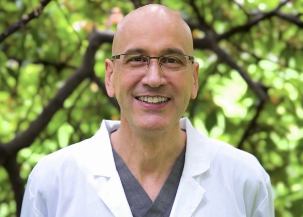 Dr. John C Dolan, orthodontist, smiling in front of foliage at his NYC practice.